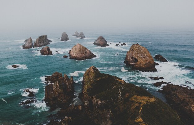 Disparo de alto ángulo de grandes rocas en nugget point ahuriri, nueva zelanda con un fondo brumoso