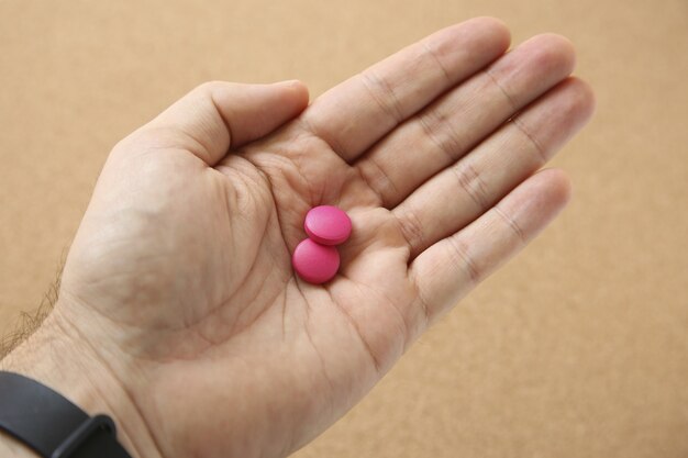 Disparo de alto ángulo de la mano de un ser humano con dos pastillas de color rosa sobre rosa