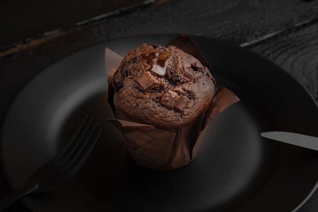 Disparo de alto ángulo de un muffin de chocolate sobre una placa negra sobre una mesa de madera oscura.