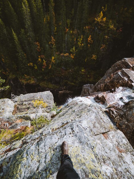 Disparo de alto ángulo de una persona de pie sobre una roca en la cima de una cascada en Noruega