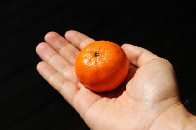 Disparo de alto ángulo de una persona sosteniendo una mandarina sobre un fondo oscuro