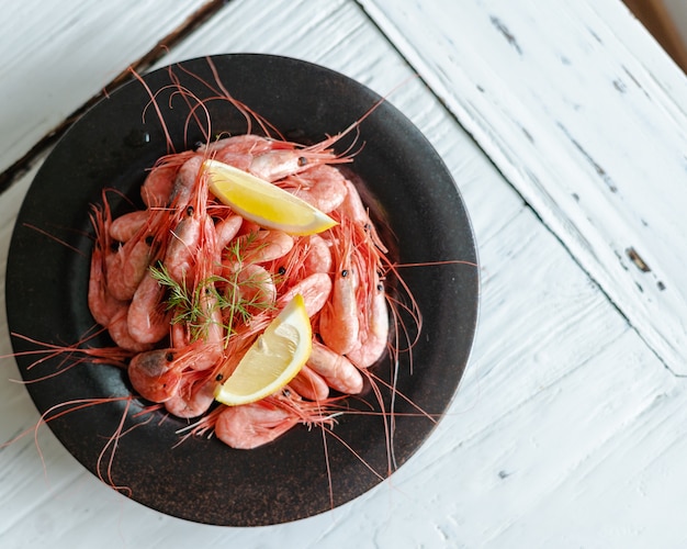 Foto gratuita disparo de alto ángulo de un plato de camarones botan con limón sobre una superficie de madera blanca