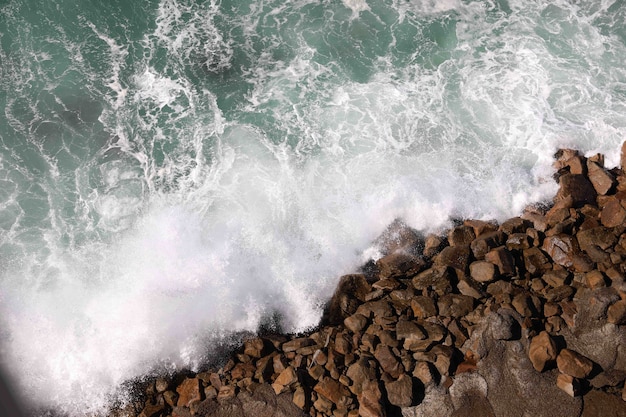 Foto gratuita disparo de alto ángulo de salpicaduras de agua sobre las rocas de la playa