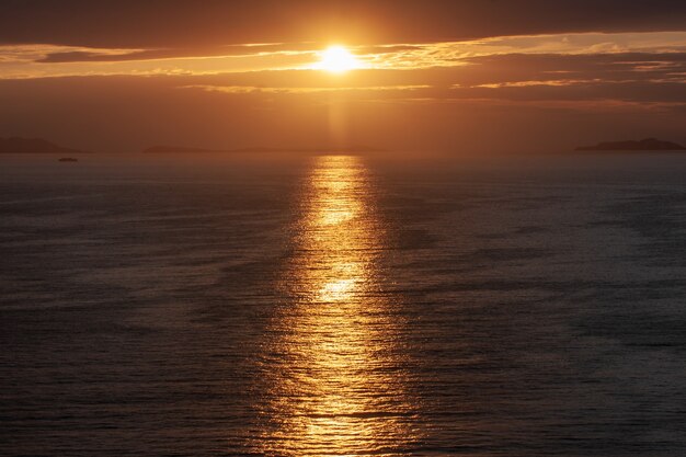 Disparo de alto ángulo del sol que brilla desde detrás de las nubes, reflejándose en el mar