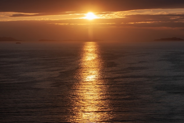 Disparo de alto ángulo del sol que brilla desde detrás de las nubes, reflejándose en el mar