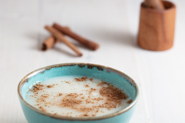 Disparo de alto ángulo de una taza de leche con canela y algunas ramas de canela sobre una superficie blanca