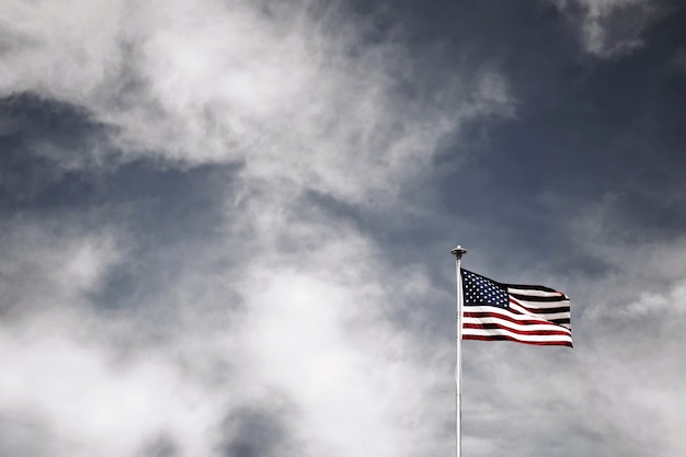 Disparo de ángulo bajo de la bandera americana en un poste bajo el cielo nublado