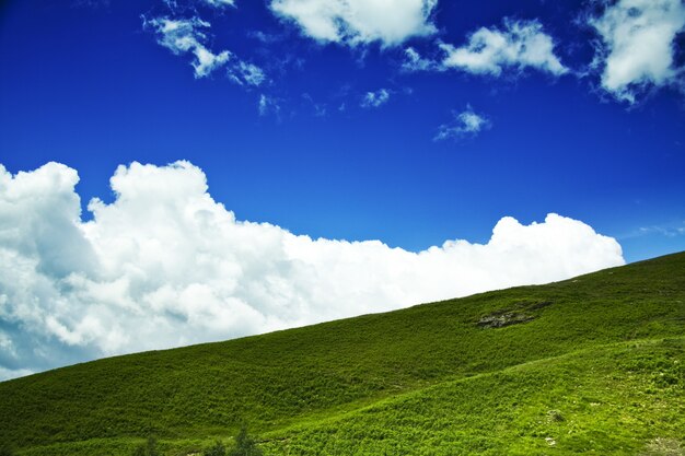 Disparo de ángulo bajo de una colina verde con un nublado cielo azul de fondo