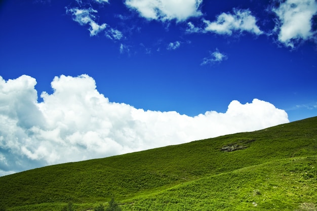 Disparo de ángulo bajo de una colina verde con un nublado cielo azul de fondo