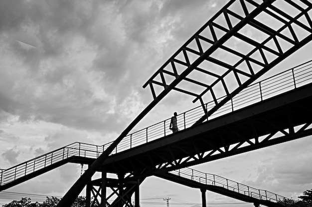 Disparo de ángulo bajo en escala de grises de un hombre caminando a través de un puente