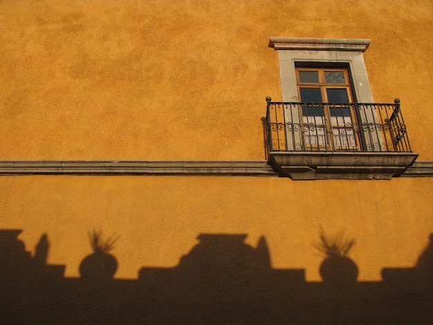 Foto gratuita disparo de ángulo bajo de una ventana de vidrio con una valla metálica y sombras en una pared amarilla de un edificio