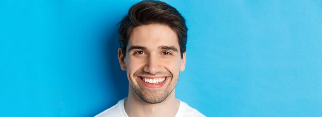 Disparo a la cabeza de un apuesto joven con barba sonriendo feliz sobre el espacio de copia de fondo azul