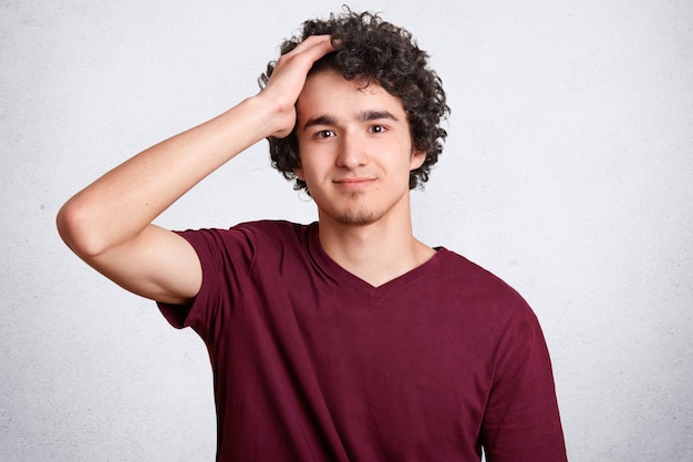 Disparo en la cabeza del apuesto joven, tiene el cabello rizado, mantiene la mano sobre la cabeza