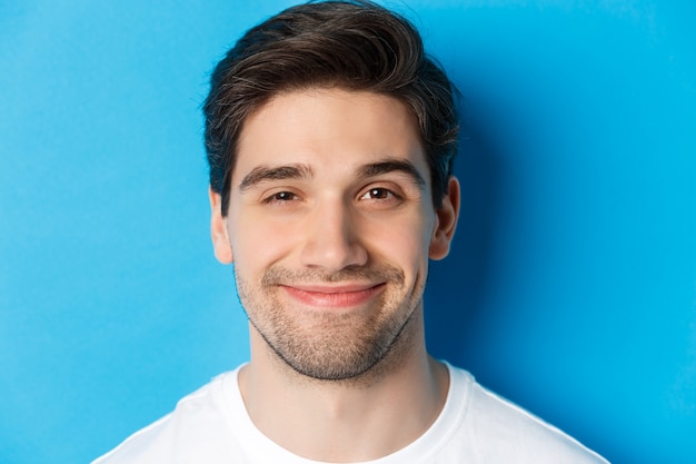 Disparo en la cabeza del hombre atractivo sonriendo complacido, mirando intrigado, de pie sobre fondo azul.