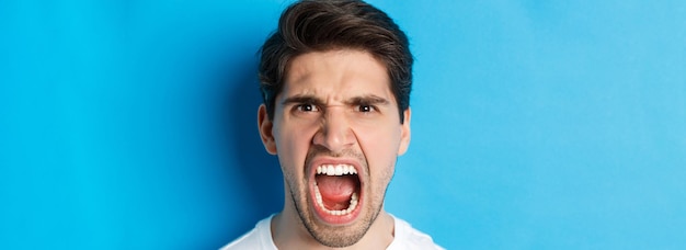 Foto gratuita disparo a la cabeza del hombre enojado gritando y mirando con odio de pie loco contra el fondo azul.