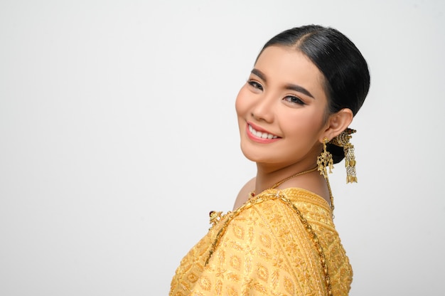 Disparo en la cabeza, retrato Hermosa mujer asiática en traje de traje tradicional tailandés sonríe y posa con gracia en la pared blanca