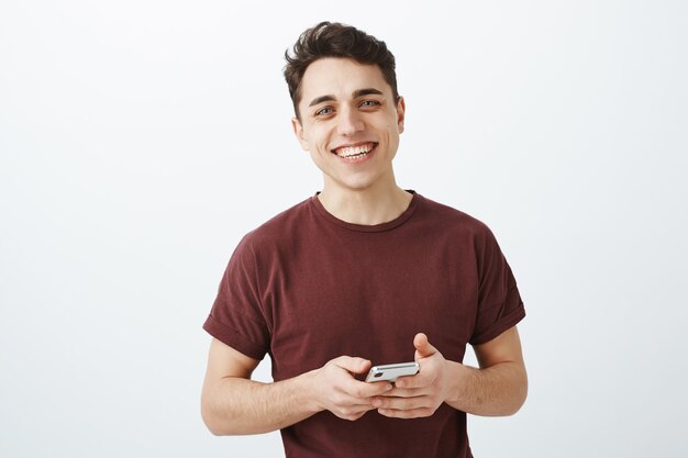 Disparo de cintura para arriba del despreocupado estudiante saliente en camiseta roja casual con smartphone