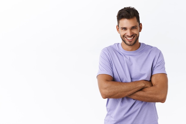 Disparo en la cintura a un hombre caucásico guapo y saludable masculino con cerdas en camiseta morada con los brazos cruzados sobre el pecho sonriendo con expresión satisfecha y despreocupada con una charla informal y alegre