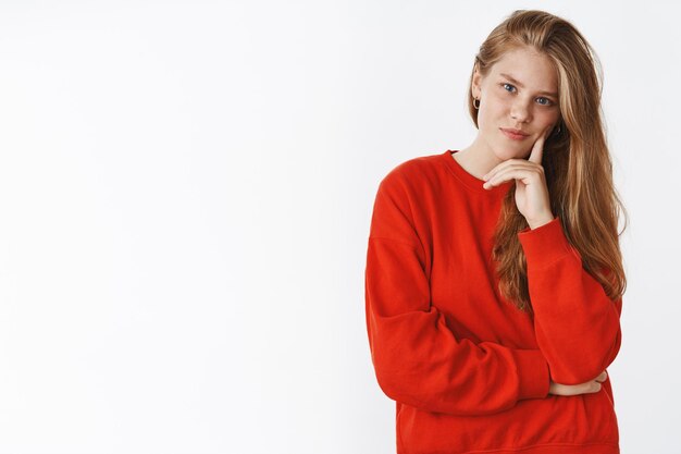 Disparo de cintura de intrigada inteligente y creativa apuesto joven europeo con largo cabello rubio natural en suéter rojo