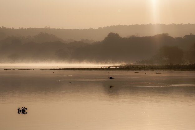 Disparo de color sepia de agua del lago rodeado de árboles y montañas