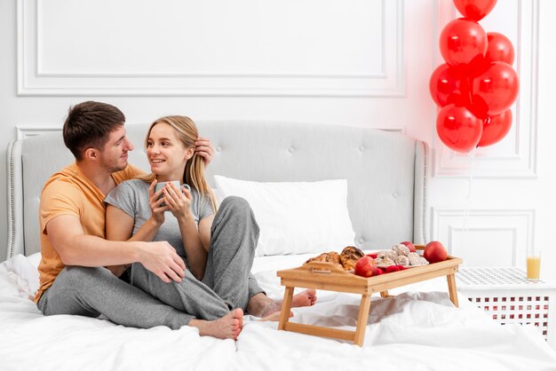 Disparo completo feliz pareja en la cama con desayuno