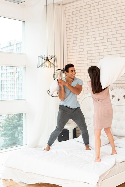 Disparo completo feliz pareja peleando con almohadas en la cama