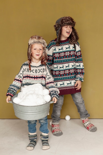 Foto gratuita disparo completo niños felices jugando con bolas de nieve en el interior