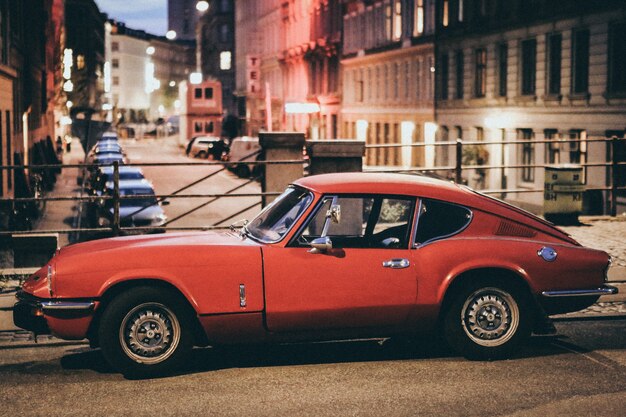 Disparo de enfoque selectivo de un automóvil Porsche rojo estacionado cerca de edificios en un fondo borroso