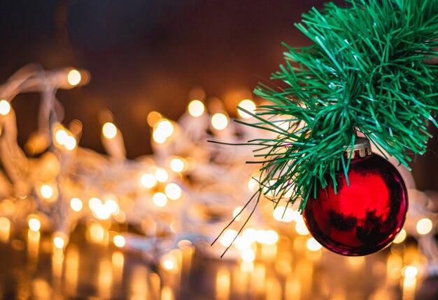 Disparo de enfoque selectivo de una bola roja de Navidad en un pino con luces en el fondo
