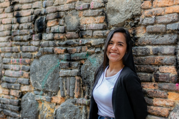 Foto gratuita disparo de enfoque selectivo de una joven mujer colombiana feliz apoyado contra una pared de ladrillos