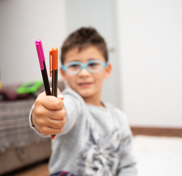 Disparo de enfoque selectivo de un niño con gafas mostrando los marcadores de colores