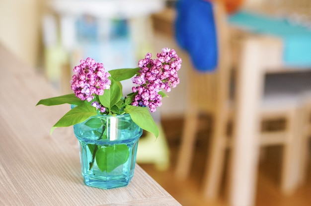 Disparo de enfoque selectivo de ramitas de flor lila en un vaso con agua en la mesa de madera