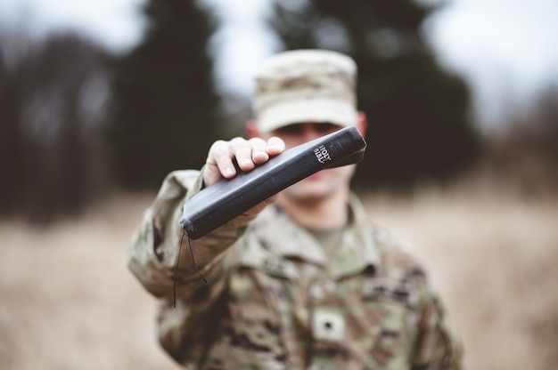 Foto gratuita disparo de enfoque selectivo de un soldado estadounidense sosteniendo la santa biblia cerca de la cámara