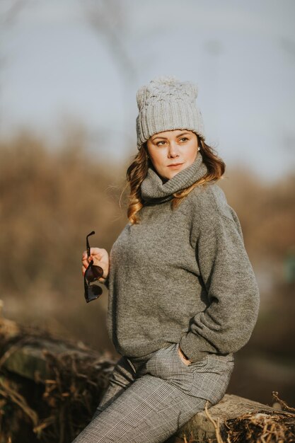 Disparo de enfoque selectivo vertical de una señorita vistiendo un suéter de cuello alto gris, pantalones y un sombrero