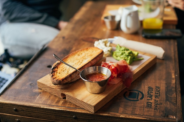 Disparo de enfoque suave del hombre que tiene un delicioso desayuno enorme en un restaurante o café fresco, pone guacamole o aguacate encima de una tostada de pan de centeno