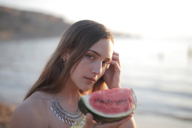 Foto gratuita disparo de enfoque superficial de una atractiva mujer sosteniendo un melón mientras mira a la cámara
