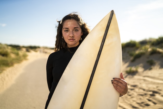 Disparo de enfoque superficial de una atractiva mujer sosteniendo una tabla de surf en medio de la carretera en España