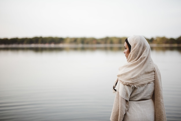 Foto gratuita disparo de enfoque superficial desde detrás de una mujer vistiendo una bata bíblica mientras mira en la distancia
