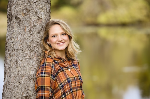 Disparo de enfoque superficial de una hermosa mujer apoyada contra un árbol y sonriendo a la cámara