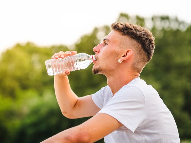 Disparo de enfoque superficial de un hombre caucásico de agua potable después de un entrenamiento en un parque