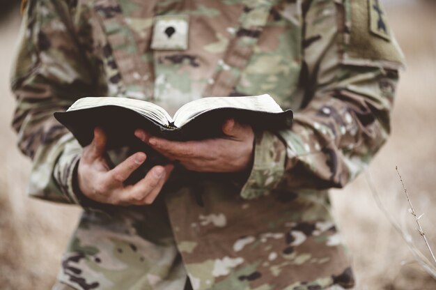 Disparo de enfoque superficial de un joven soldado sosteniendo una Biblia abierta en un campo