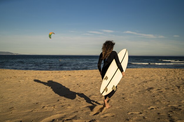 Disparo de enfoque superficial de una mujer que lleva una tabla de surf mientras camina a la orilla del mar en España