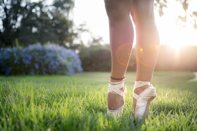 Disparo de enfoque superficial de los pies de una bailarina de ballet de pie sobre la hierba verde