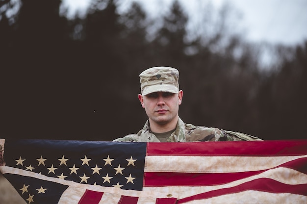 Foto gratuita disparo de enfoque superficial de un soldado estadounidense sosteniendo la bandera estadounidense