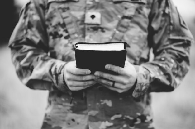 Disparo en escala de grises de un joven soldado sosteniendo una Biblia