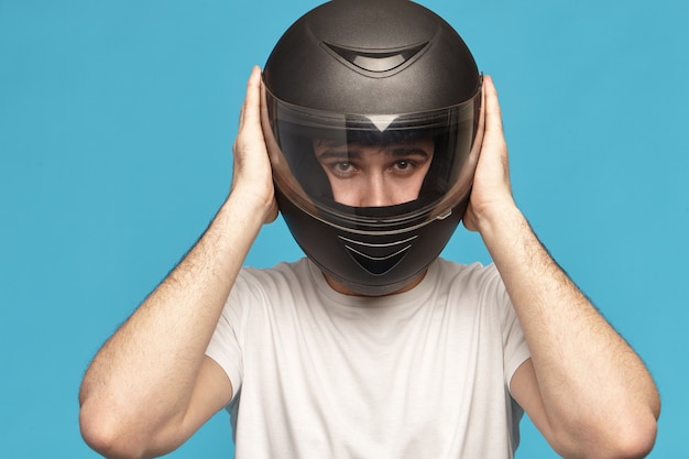 Foto gratuita disparo de estudio aislado de motorista masculino caucásico joven serio autodeterminado tomando elegante casco de motocicleta negro