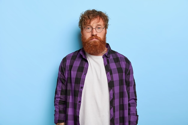 Foto gratuita disparo de estudio de guapo serio elegante ginger guy posando contra la pared azul