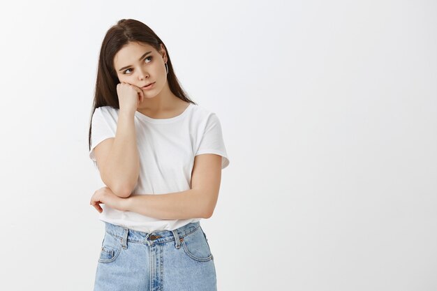 Disparo de estudio de triste mujer joven aburrida posando contra la pared blanca