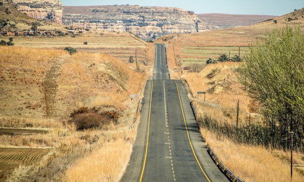 Disparo de gran angular de una carretera que va en una montaña rodeada de arbustos y pasto seco