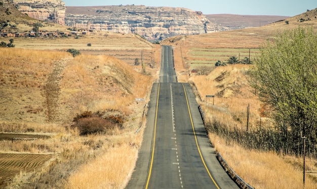 Disparo de gran angular de una carretera que va en una montaña rodeada de arbustos y pasto seco